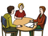 Leichte Sprache Bild: Drei Menschen um einen Tisch, rechts eine Frau, die den anderen beiden Personen etwas erklärt